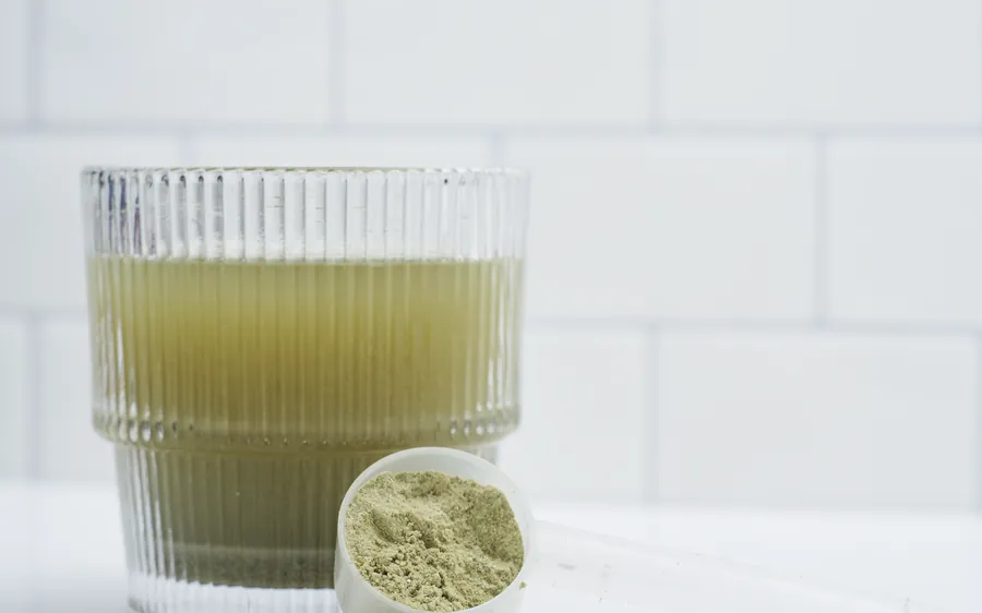 A ribbed glass of mixed Bondi Pure beside a scoop of the green powder on a white kitchen counter.
