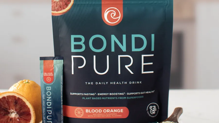 Bondi Pure Blood Orange pouch and stick pack on a kitchen counter with fresh blood oranges and a wooden scoop of the powder.